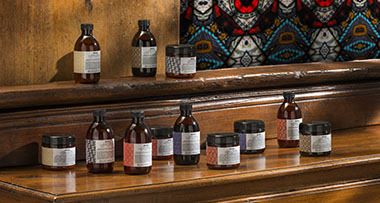 A hand reaching for a dropper bottle in a display of hair care products, featuring numbered bottles with labels, on a countertop with greenery and a mirror. Ideal for those exploring hair care solutions in their beauty routine.