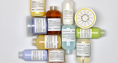 A collection of grooming products on a bathroom countertop, featuring various bottles and tubes with yellow labels, along with a brush and a small mirror, arranged on a marble surface.