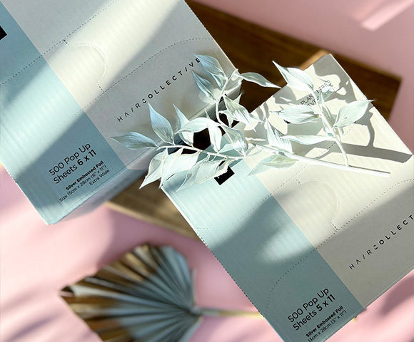 Packaged hair product pop-up sheets arranged with decorative foliage, showcasing minimalist design and branding.