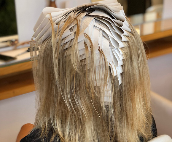 A stylist is sectioning hair using a paper guide for a haircut or coloring technique, focusing on precise lines and layering.