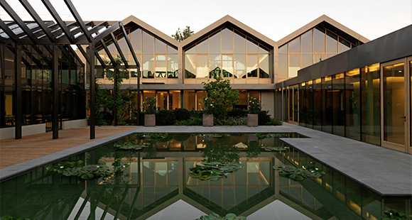 Modern architectural courtyard featuring a serene reflecting pool with lily pads, surrounded by lush greenery and contemporary buildings.